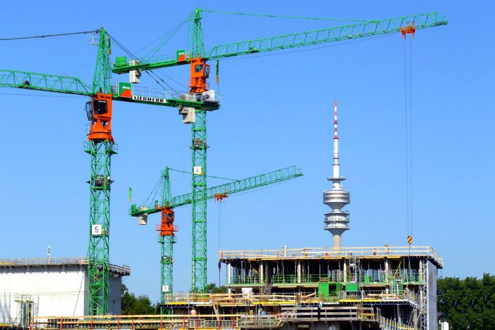 Baustelle mit drei Kränen in München. Im Hintergrund ist der Fernsehturm zu sehen.