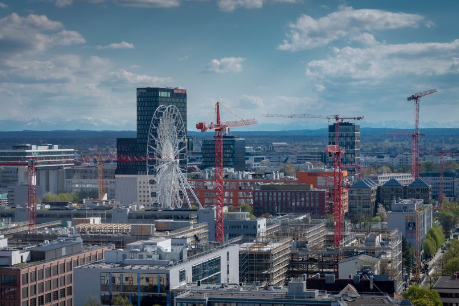 Blick auf das Münchner Werksviertel mit einigen Gebäuden noch im Bau und im Hintergrund die Bergkette bei Fön