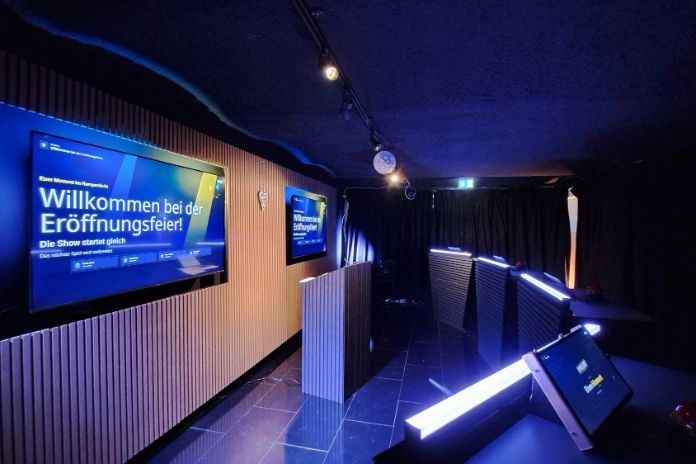 Raum mit gedimmtem Licht, Fernsehern an der Wand und Podien mit Tablets gegenüber