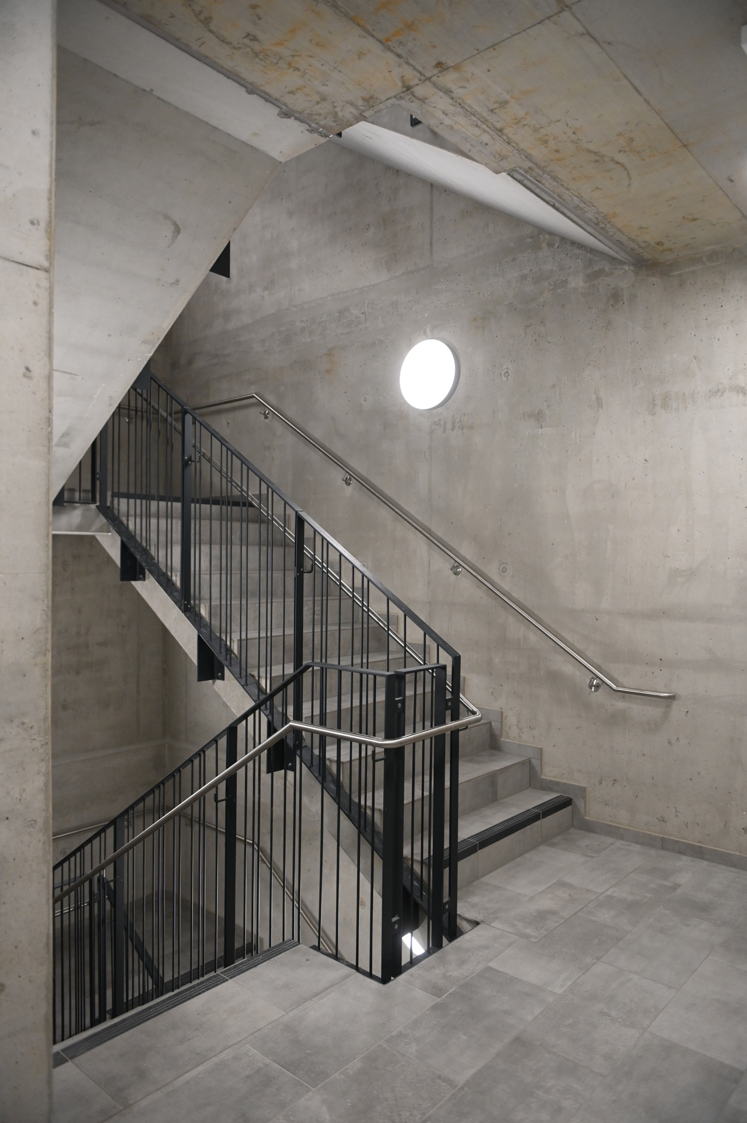 Treppenhaus mit Rohbeton-Wänden und Treppe mit schwarzem Geländer