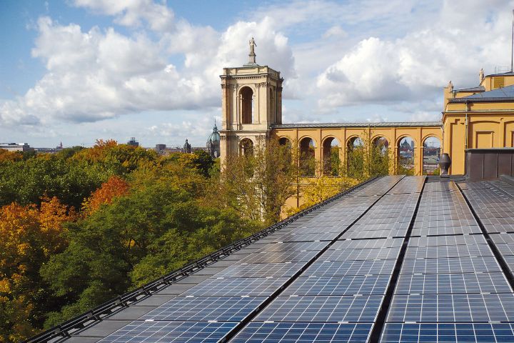 Blick auf die Solarpaneele auf dem Dach des Münchner Maximilianeums, dahinter die Gebäudefront und Bäume an der Isar